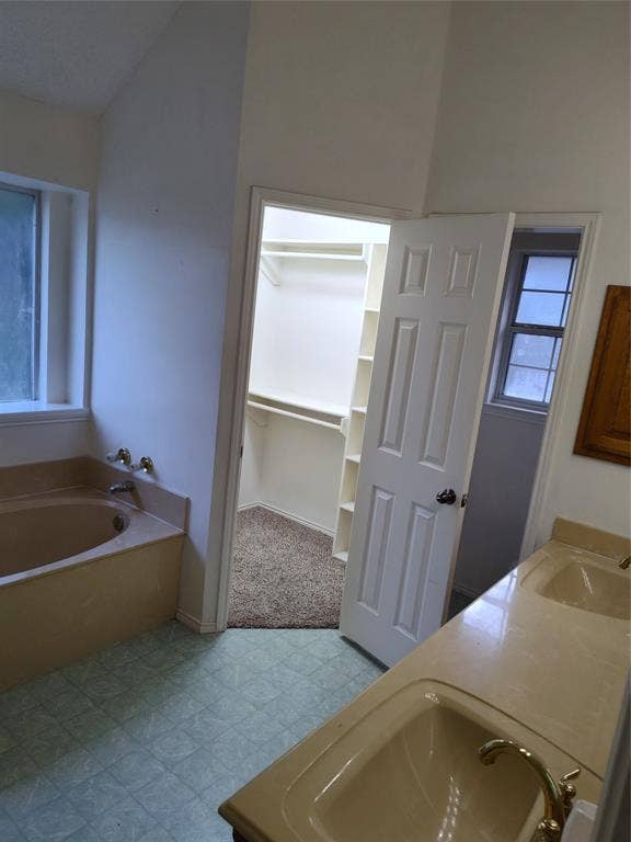 Dual-sink vanity with a solid-surface countertop, jetted soaking tub, multi-panel interior door, and walk-in closet with built-in shelving