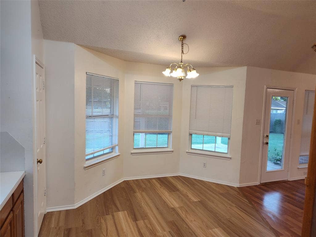 Vaulted ceiling, bay-style window arrangement, wood-finish flooring, multi-light chandelier, and glass-paneled exterior door