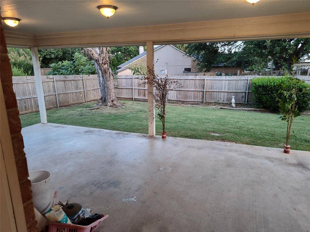 Covered concrete patio with recessed ceiling lighting and a fenced-in backyard featuring a grass lawn and mature trees