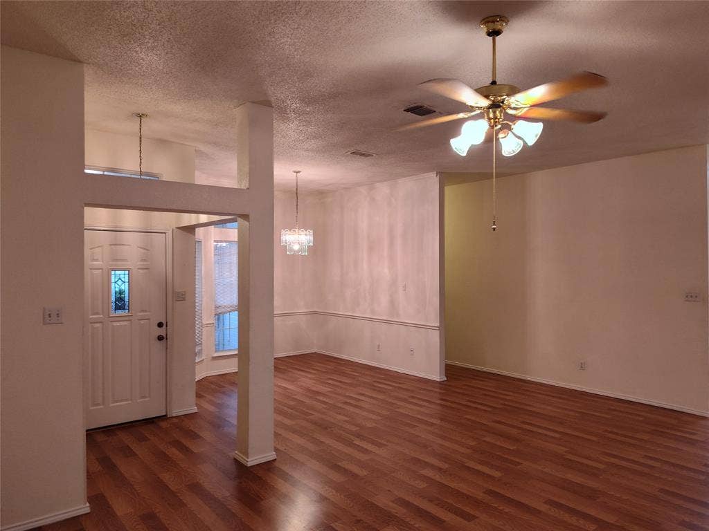 Wood-finish flooring, high ceilings, ceiling fan with light fixture, decorative multi-light chandelier, and front door with glass inlay
