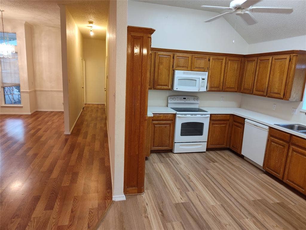 Kitchen featuring wood cabinetry, white appliances, wood-finish flooring, and a vaulted ceiling with a mounted ceiling fan