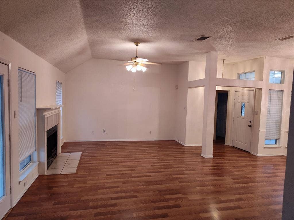 Vaulted ceilings, wood-finish flooring, built-in fireplace with tile surround, ceiling fan with light kit, and natural light via multiple windows