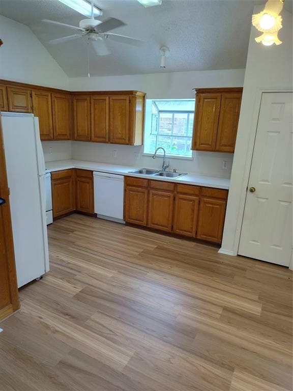 Kitchen featuring wood cabinetry, solid-surface countertops, dual-basin stainless steel sink, wood-finish flooring, and vaulted ceiling