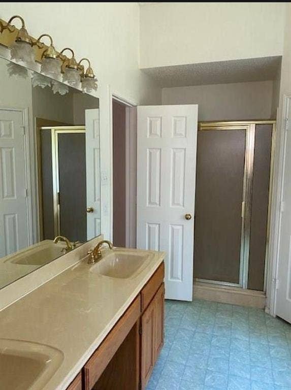 Double vanity featuring a solid-surface countertop with integrated sinks, metallic finish fixtures, a multi-bulb light fixture, and a walk-in shower with metal-framed glass doors