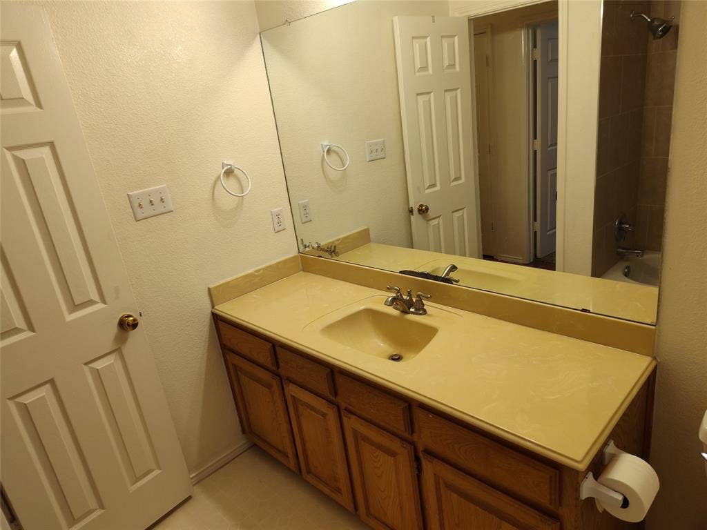 Vanity featuring wood-finish cabinetry, an integrated solid-surface countertop and basin, a large wall-mounted mirror, and multi-panel interior doors