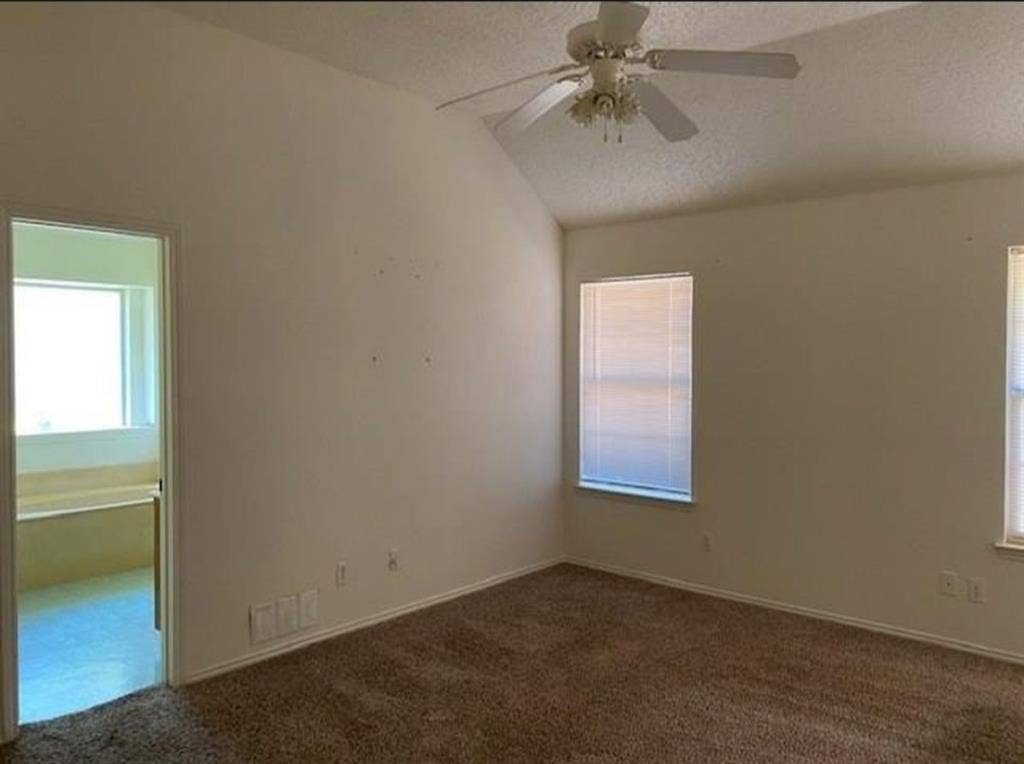 Vaulted ceilings featuring a central white ceiling fan with multi-light fixture, neutral carpeting, and large windows with integrated blinds