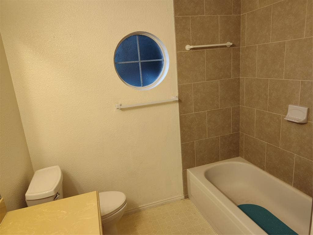 Bathroom featuring a circular accent window, a bathtub with full-height tile surround, and a built-in soap dish