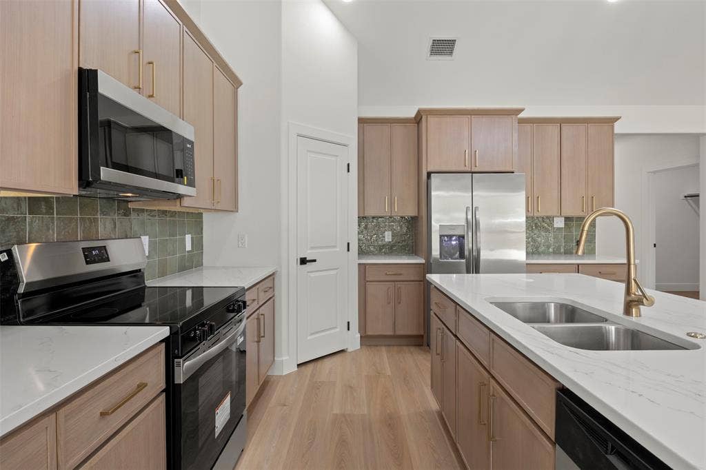 2507 Picadilly Boulevard, Mesquite, TX 75149 Kitchen featuring wood-finish cabinetry, stainless steel appliances, white countertops, a dual basin sink with a gold-finish faucet, and a green tile backsplash