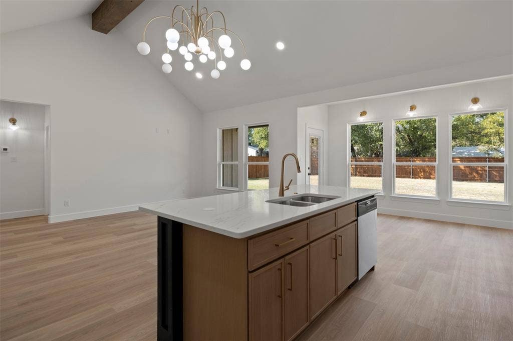 2507 Picadilly Boulevard, Mesquite, TX 75149 Vaulted ceiling with an exposed wood beam, contemporary chandelier, wood-finish flooring, kitchen island with a double basin sink and integrated dishwasher, and multiple large windows