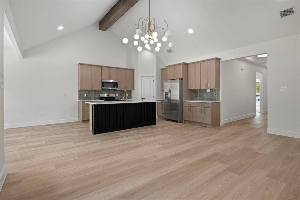 2507 Picadilly Boulevard, Mesquite, TX 75149 Vaulted ceiling with exposed wood beam, wood-finish flooring, kitchen island with dark paneling, light wood cabinetry, and stainless steel appliances