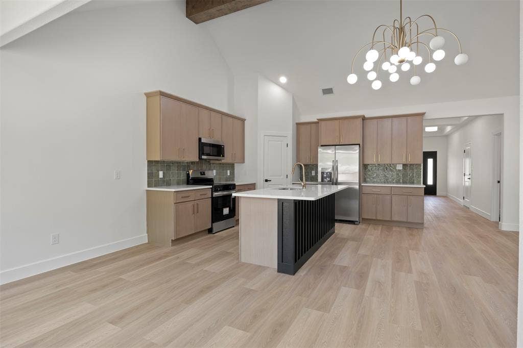 2507 Picadilly Boulevard, Mesquite, TX 75149 Vaulted ceiling with exposed wood beam, kitchen island with fluted paneling, stainless steel appliances, light wood-finish flooring, and modern chandelier