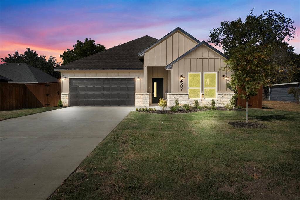 2507 Picadilly Boulevard, Mesquite, TX 75149 Modern exterior featuring vertical board and batten siding, stone facade accents, a dark-paneled garage door, and a concrete driveway