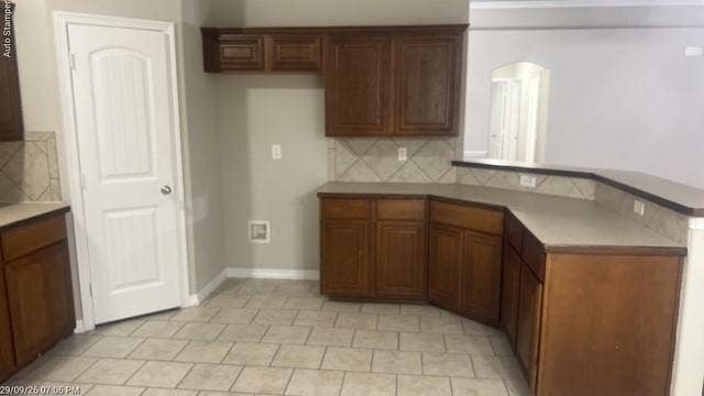Wood-finish cabinetry, tile flooring, tile backsplash, and a multi-level countertop