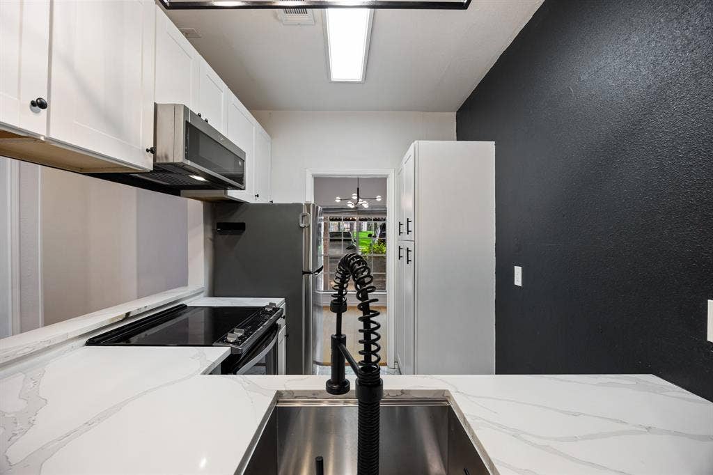 9801 Royal Lane, #701, Dallas, TX 75231 White shaker-style cabinetry with dark hardware, stainless steel appliances, white patterned countertops, stainless steel undermount sink, and a black gooseneck pull-down faucet