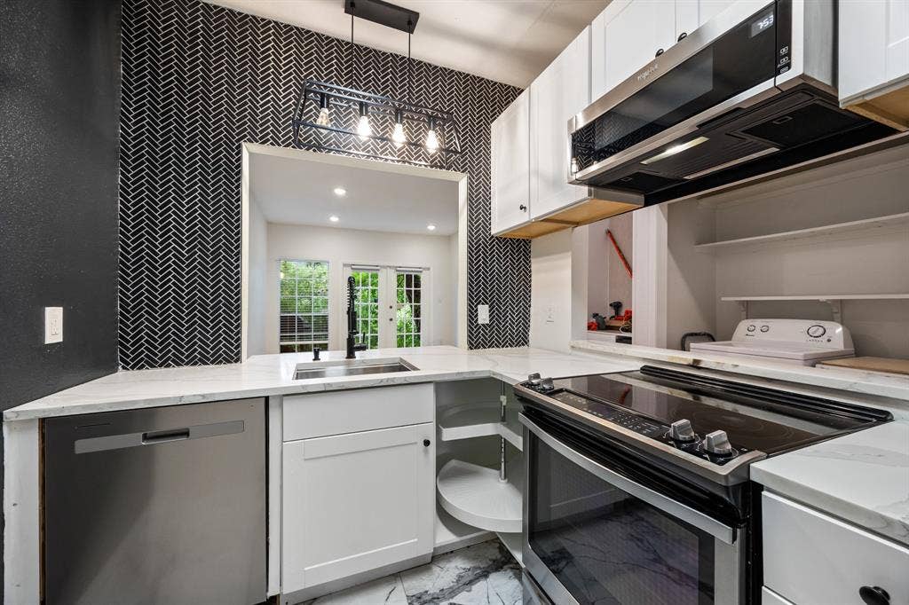 9801 Royal Lane, #701, Dallas, TX 75231 Kitchen featuring white cabinetry, light countertops, stainless steel appliances, and a black herringbone tile accent wall