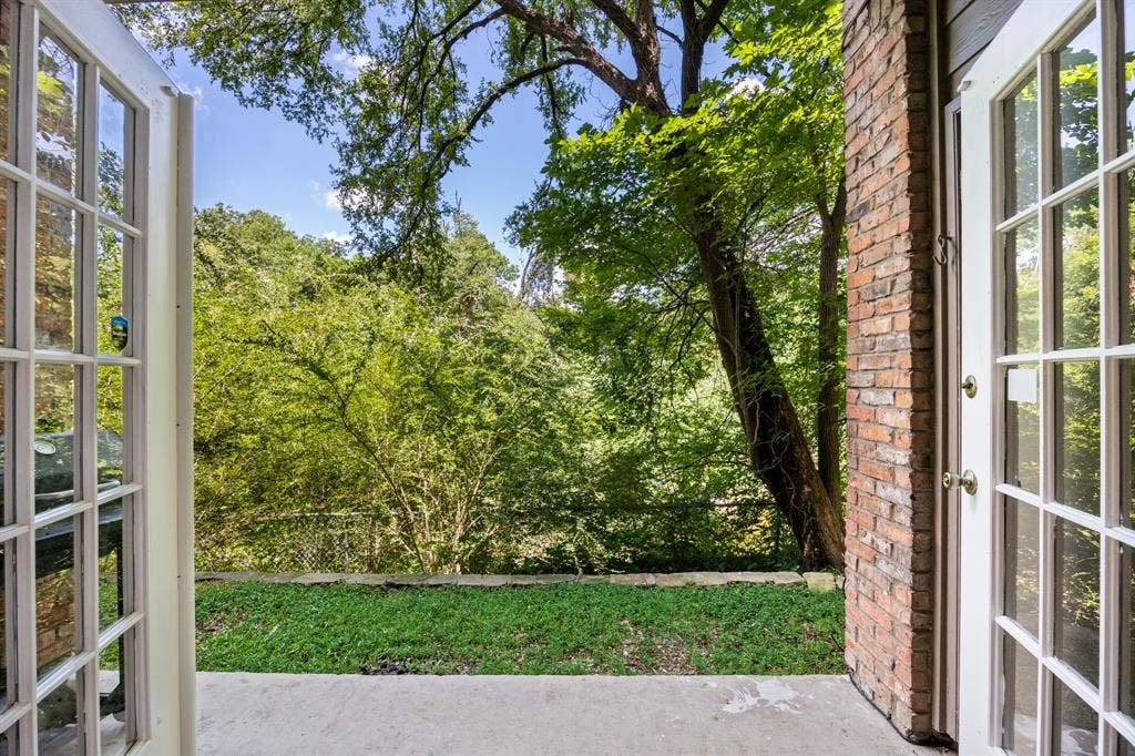 9801 Royal Lane, #701, Dallas, TX 75231 Patio with concrete flooring, brick exterior wall, and double French doors opening to a grassy area and mature trees