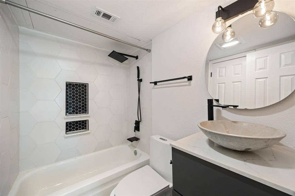 9801 Royal Lane, #701, Dallas, TX 75231 White hexagonal wall tile, dual shower niches with mosaic tile, black matte rainfall showerhead, vessel sink, and a black vanity with a white countertop