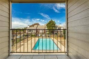5726 Marvin Loving Drive, #221, Garland, TX 75043 Balcony with metal railing and a concrete floor, overlooking a swimming pool with a surrounding paved area, and distant buildings with pitched roofs