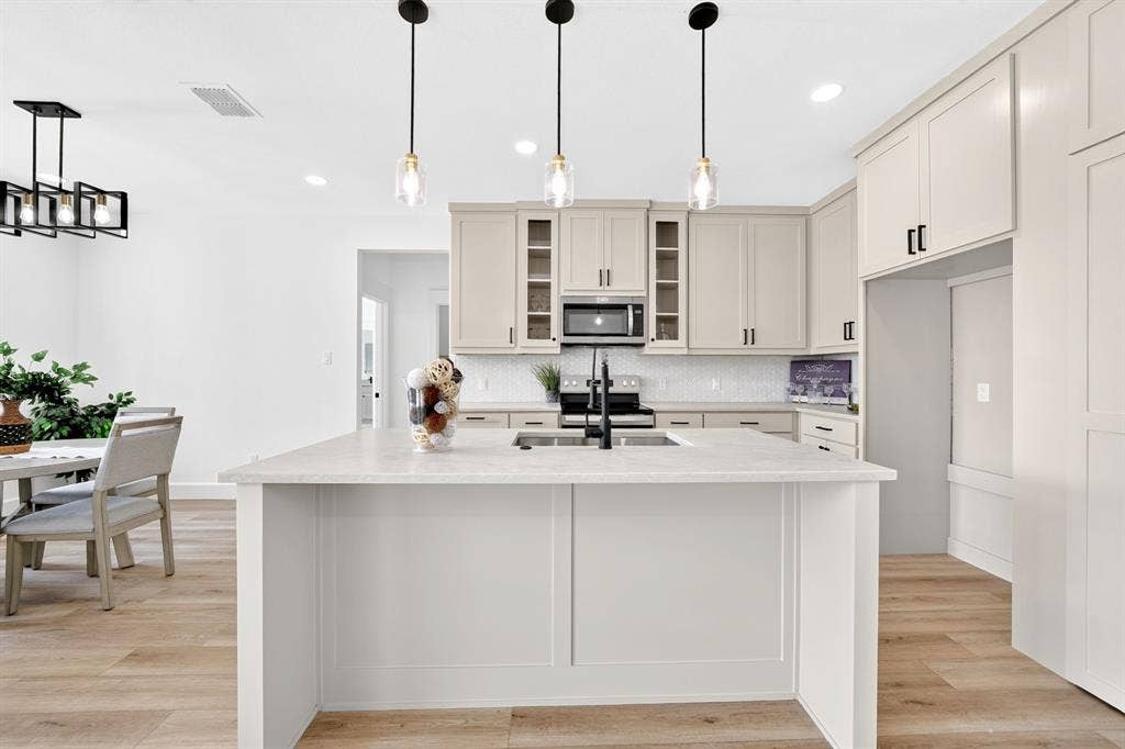 5731 Lewis Court, Athens, TX 75752 Kitchen island with a light-toned countertop, pendant lighting, built-in microwave, white subway tile backsplash, and light-toned cabinetry with dark hardware