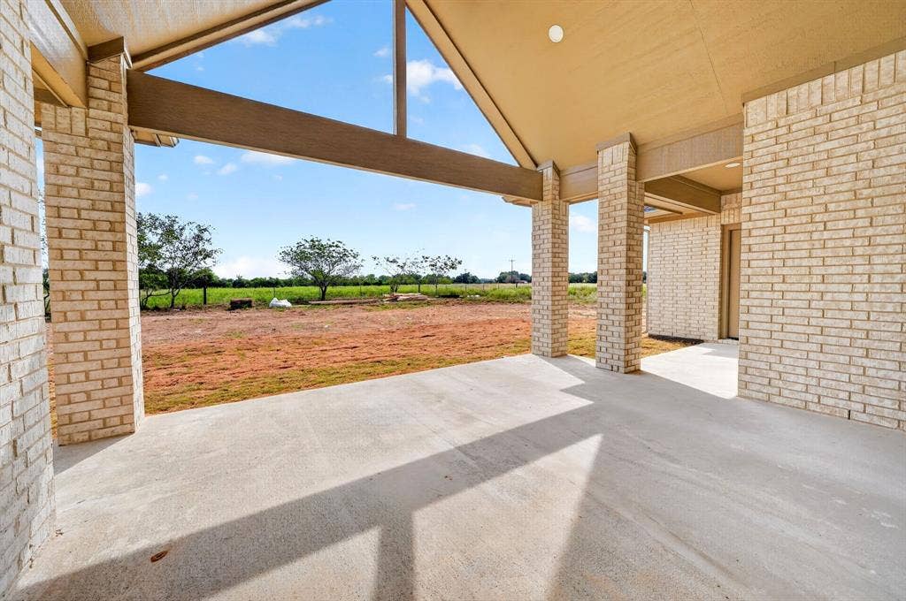 5731 Lewis Court, Athens, TX 75752 Expansive covered concrete patio with brick pillars, exposed beam ceiling, and a broad open-sky backdrop