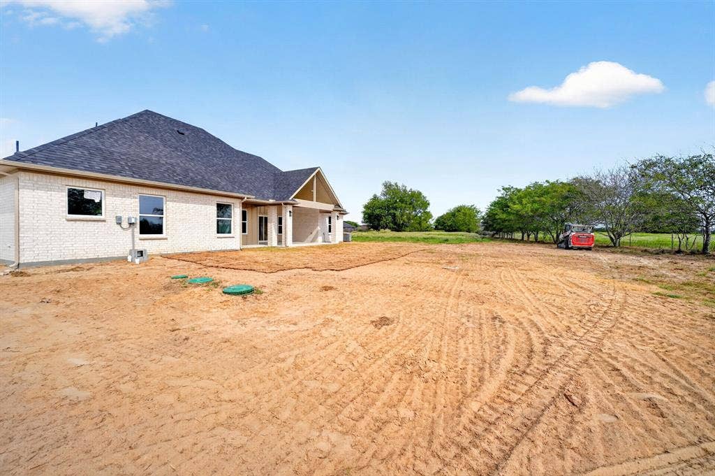 5731 Lewis Court, Athens, TX 75752 Rear exterior with white brick facade, dark shingle roof, and covered patio