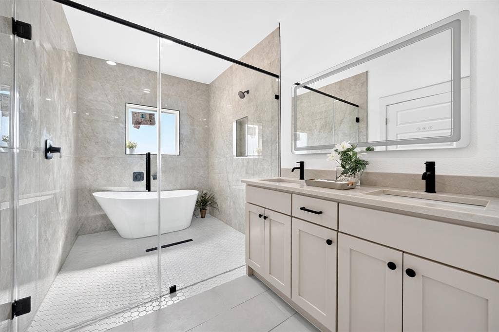5731 Lewis Court, Athens, TX 75752 Dual vanity with undermount sinks and matte black fixtures, an illuminated mirror, a freestanding soaking tub, a walk-in shower with a glass enclosure, and large format wall tiles