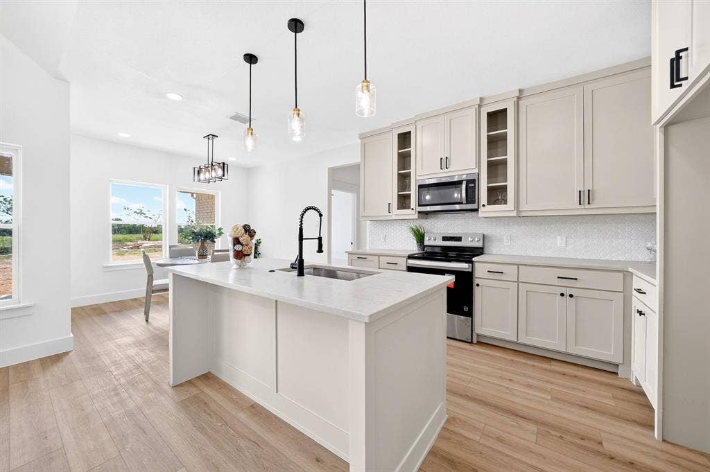 5731 Lewis Court, Athens, TX 75752 Kitchen featuring a central island with an undermount sink, light-toned cabinetry, stainless steel appliances, and wood-finish flooring