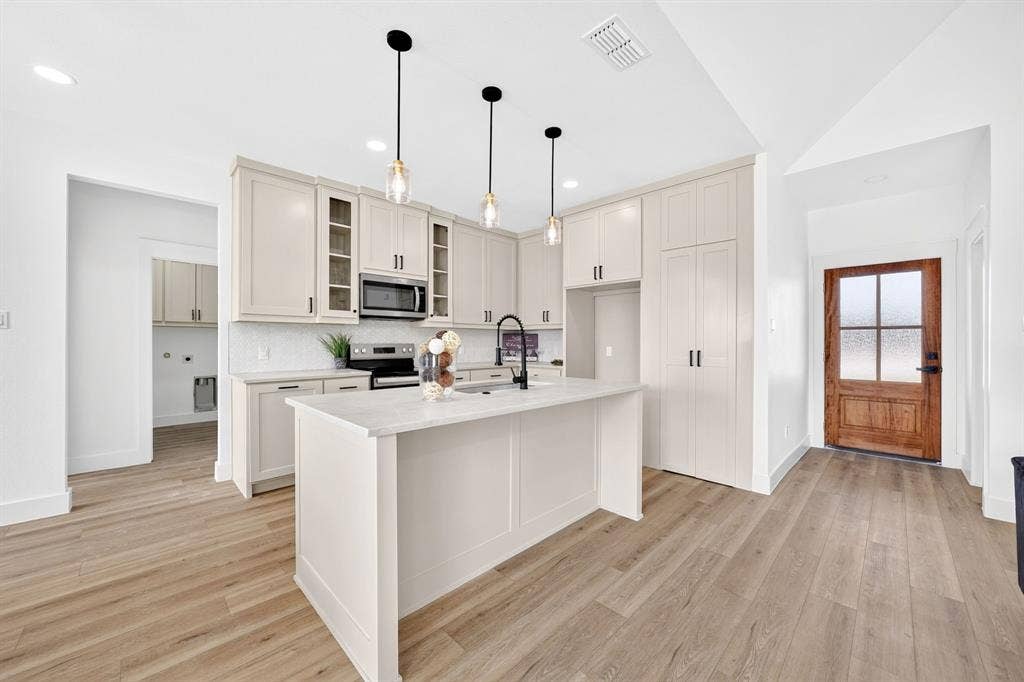 5731 Lewis Court, Athens, TX 75752 Kitchen featuring light-toned cabinetry, a central island with a countertop, wood-finish flooring, a stainless steel microwave, and pendant lighting