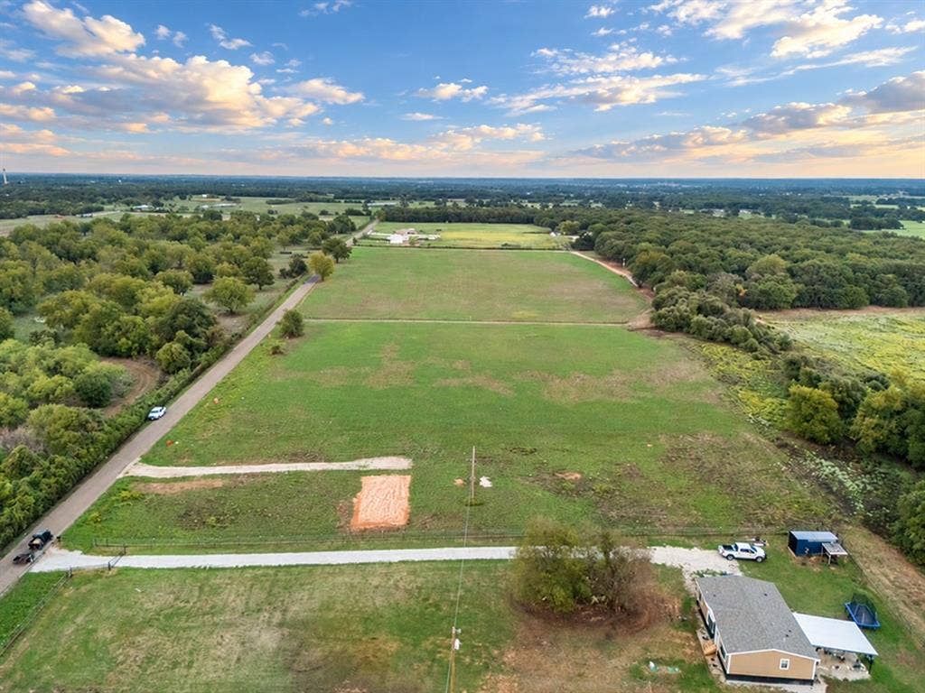 TBD MARY WARE, Waco, TX 76705 Expansive green fields bordered by mature trees and a paved road, featuring a single-story residence with a covered porch