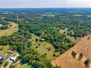 6630 Prather Road, Springtown, TX 76082 Expansive rural acreage featuring mature tree coverage, open pastureland, and a residential structure with outbuildings situated on the property