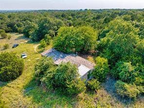 6630 Prather Road, Springtown, TX 76082 Residential structure with a shingled roof and an attached metal-roofed section, surrounded by abundant mature trees and natural landscaping