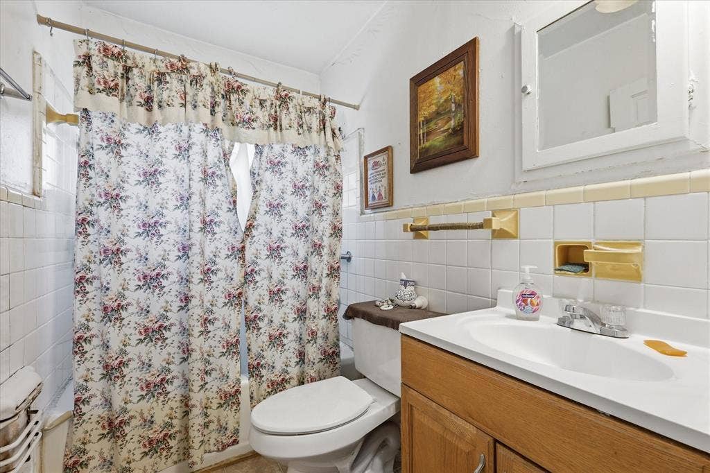 6807 Prosper Street, Dallas, TX 75209 Full bathroom with a tub/shower combination, tile surround, floral shower curtain, vanity storage, and a bright white sink area. The room offers a practical layout with essential daily function, including mirror, towel bars, built-in wall accents, and neutral tile details. Its compact footprint keeps everything within easy reach while providing the convenience of a full bath for the home.