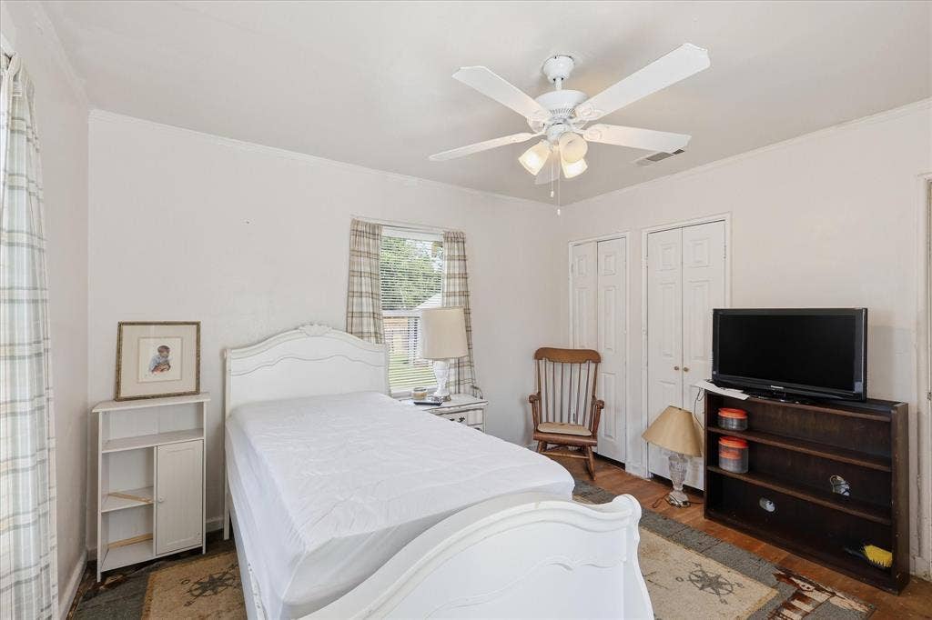 6807 Prosper Street, Dallas, TX 75209 Comfortable bedroom with white walls, ceiling fan, closet doors, wood flooring, and natural light from the window. The room includes space for a bed, side table, seating, dresser, and media furniture, offering an easy-to-use layout with multiple furnishing options. Neutral finishes help create a simple, bright backdrop ready for a buyer’s personal style.