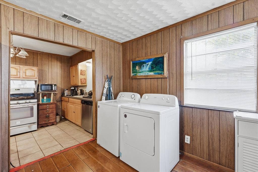 6807 Prosper Street, Dallas, TX 75209 Laundry area with washer and dryer placement, wood-paneled walls, warm wood-look flooring, and convenient access to the kitchen. This space adds valuable everyday function to the home, keeping laundry easily accessible while remaining near the main living and kitchen areas. A window brings in natural light, and the open connection to the kitchen helps the layout feel practical and efficient.