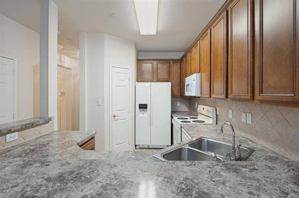 3236 Twist Trail, Plano, TX 75093 Kitchen featuring a double basin stainless steel sink, tile backsplash, wood-finish cabinetry, and white appliances