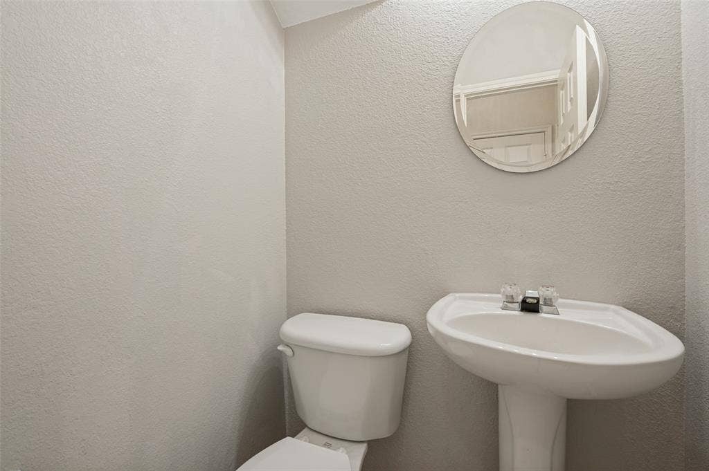 3236 Twist Trail, Plano, TX 75093 Pedestal sink with a two-handle faucet, circular wall mirror, and a white toilet