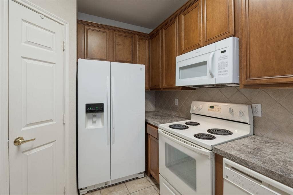 3236 Twist Trail, Plano, TX 75093 Wood-finish cabinetry, tile backsplash, white appliances, and a built-in microwave