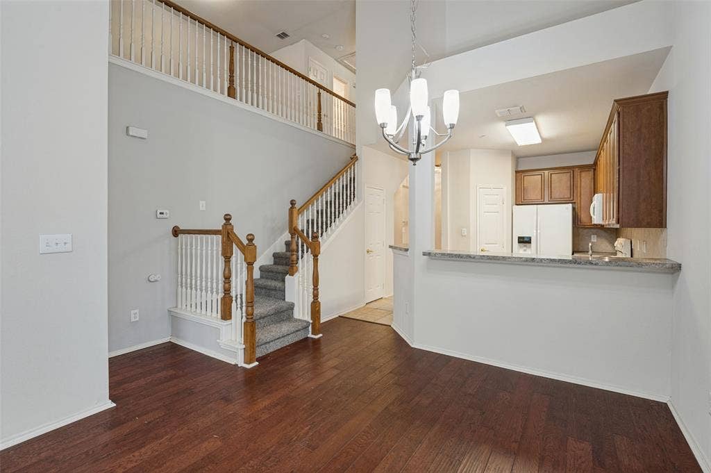 3236 Twist Trail, Plano, TX 75093 Dark wood-finish flooring, staircase with wood banister and carpeted treads, and a kitchen pass-through with stone-look countertop