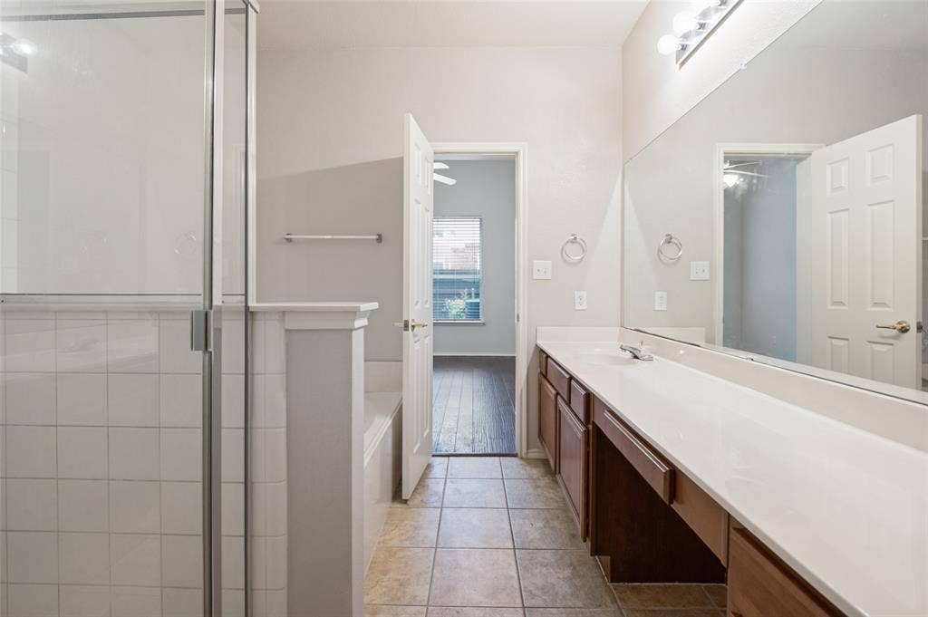 3236 Twist Trail, Plano, TX 75093 Glass-enclosed shower, built-in bathtub, extended vanity with dual sinks, wall-mounted mirror, and tile flooring