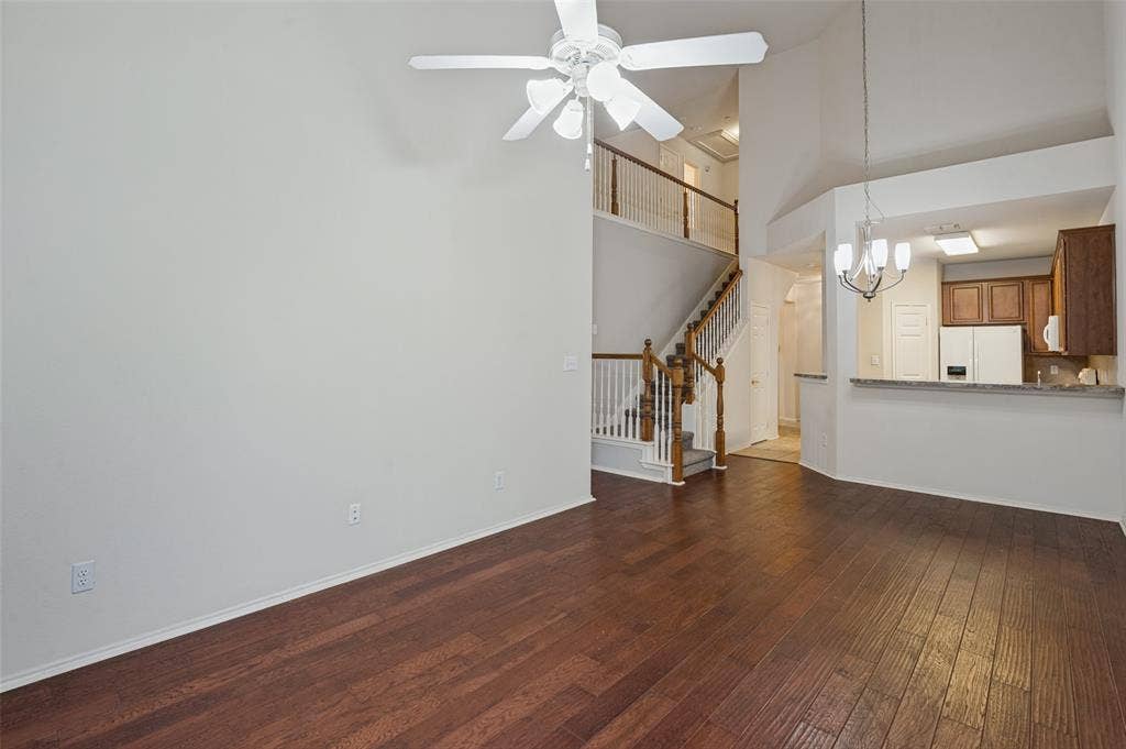 3236 Twist Trail, Plano, TX 75093 High ceilings with a ceiling fan, wood-finish flooring, staircase with wood newel posts, kitchen featuring wood cabinetry, and a breakfast bar with a stone-finish countertop