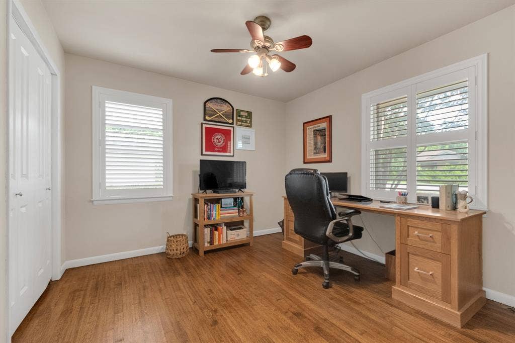 1815 Oates Drive, Dallas, TX 75228 Room featuring wood-finish flooring, two windows with white plantation shutters, and a ceiling fan with integrated lighting