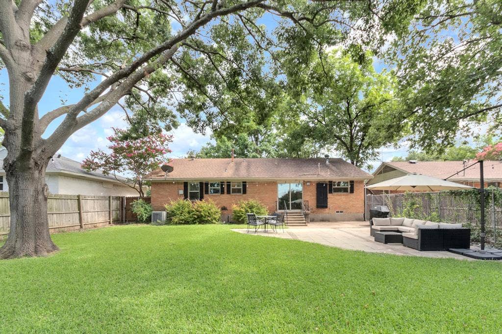 1815 Oates Drive, Dallas, TX 75228 Expansive backyard featuring a manicured lawn, large shade tree, brick exterior, full privacy fencing, and a concrete patio