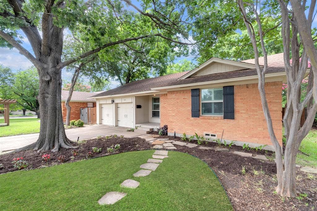 1815 Oates Drive, Dallas, TX 75228 Brick exterior with dark shutters, dual garage doors, and a stone pathway