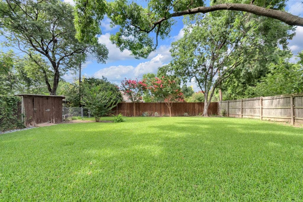 1815 Oates Drive, Dallas, TX 75228 Expansive grassy yard area featuring mature trees and a wood storage shed