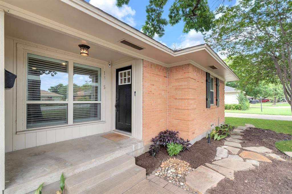 1815 Oates Drive, Dallas, TX 75228 Brick exterior featuring a black front door with decorative window inserts, an overhead porch light, and an adjacent multi-pane window