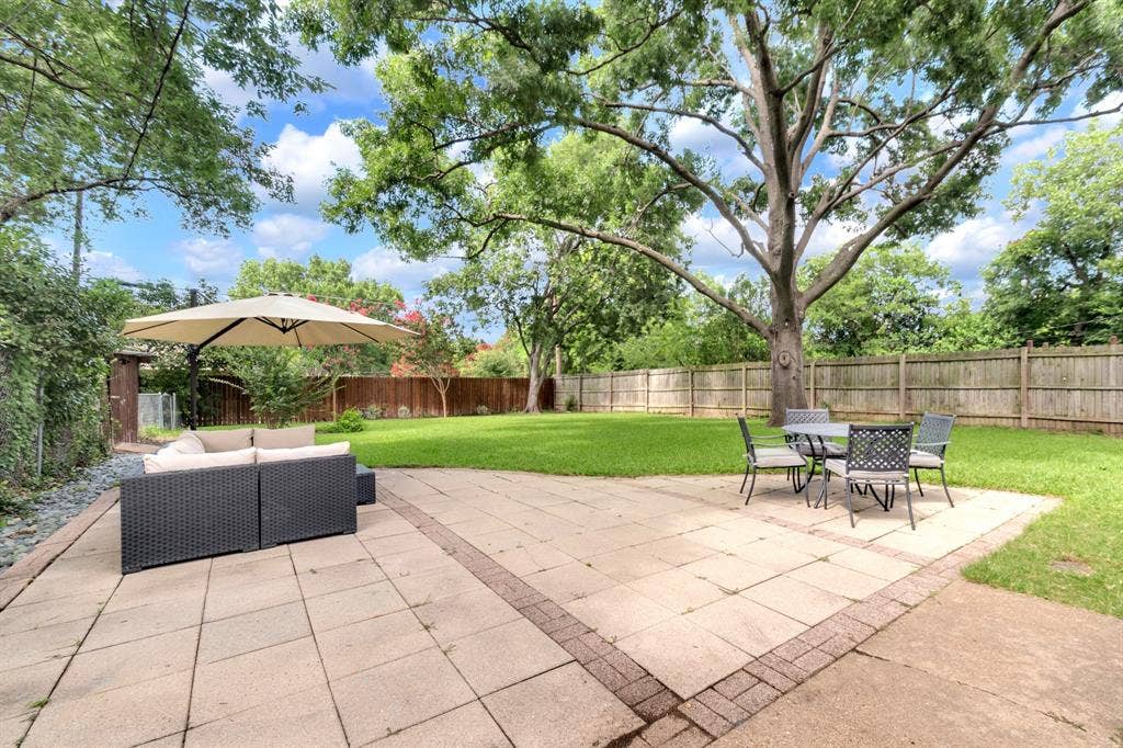 1815 Oates Drive, Dallas, TX 75228 Expansive backyard featuring a large paved patio with brick edging, a generous lawn area, mature trees, and a wood privacy fence