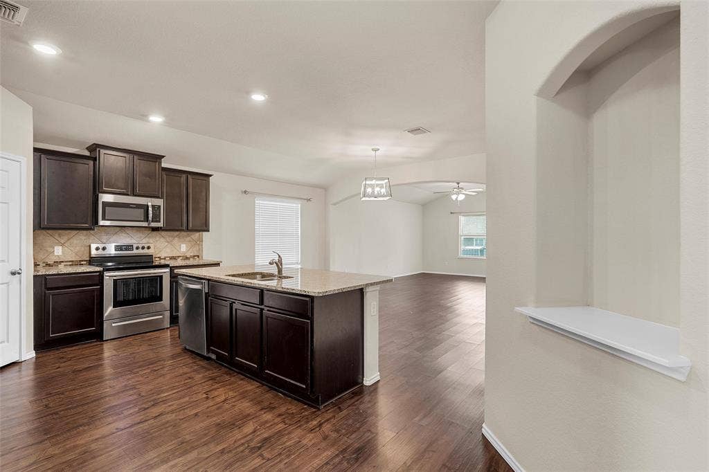 3217 Beutel Road, Lorena, TX 76655 Kitchen with appliances with stainless steel finishes, dark wood-style flooring, decorative backsplash, dark brown cabinets, and light stone countertops