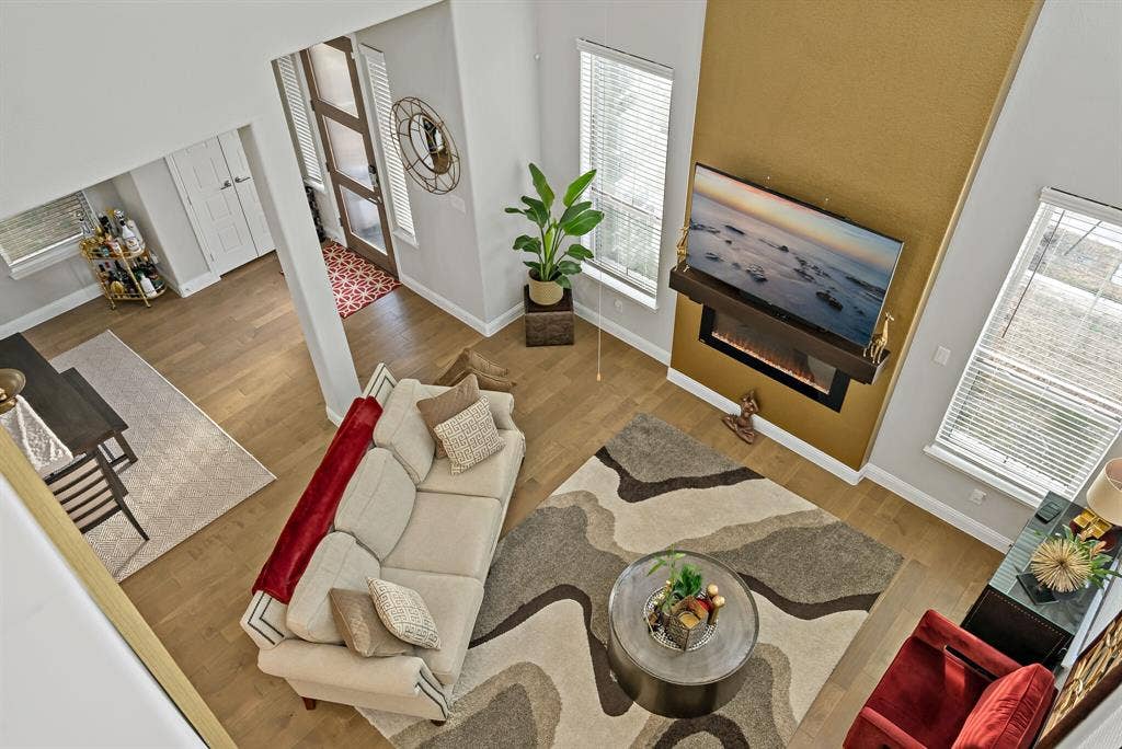 Open-concept living area featuring a two-story accent wall with an integrated electric fireplace, wood-finish flooring, and multiple windows