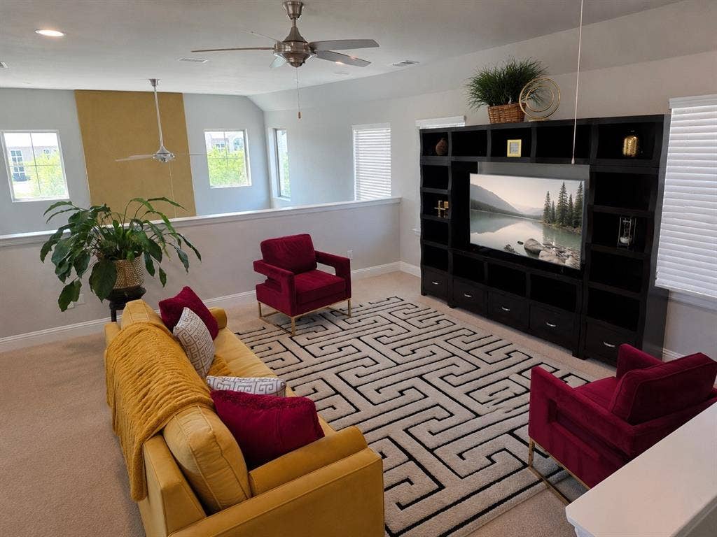 Carpeted loft area featuring a built-in media center with ample storage, multiple windows with blinds, a half-wall railing, and two ceiling fans