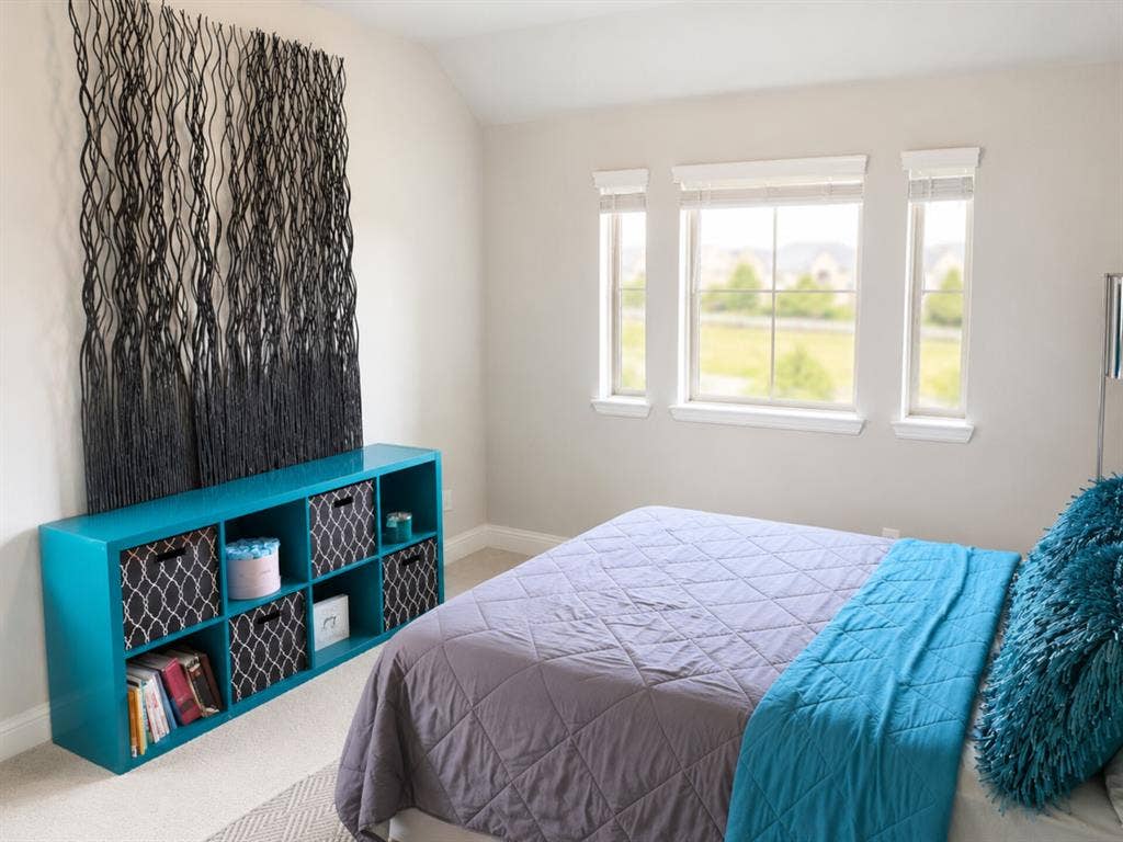 Bright secondary bedroom featuring expansive triple-pane windows with natural light, neutral wall finishes, and a built-in turquoise storage unit with open shelving and patterned cabinet doors